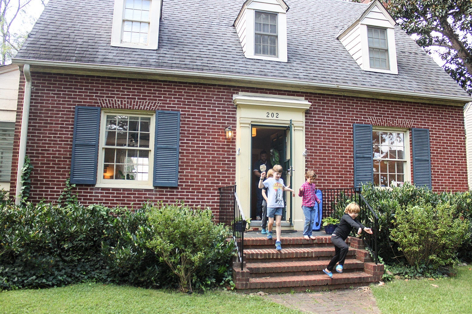 Children run out of a small house onto the lawn.