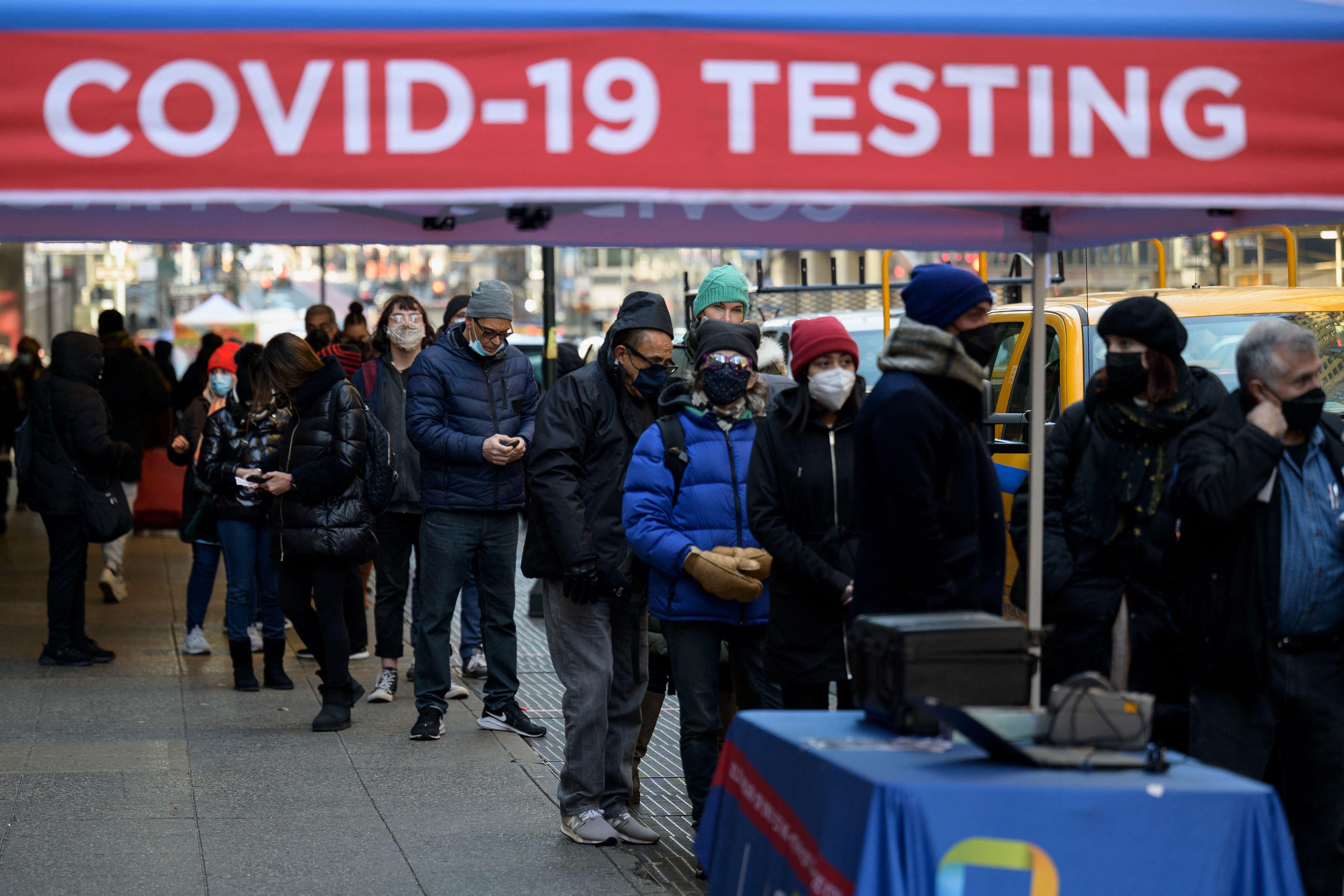 People wait in line on a sidewalk to receive a COVID-19 test