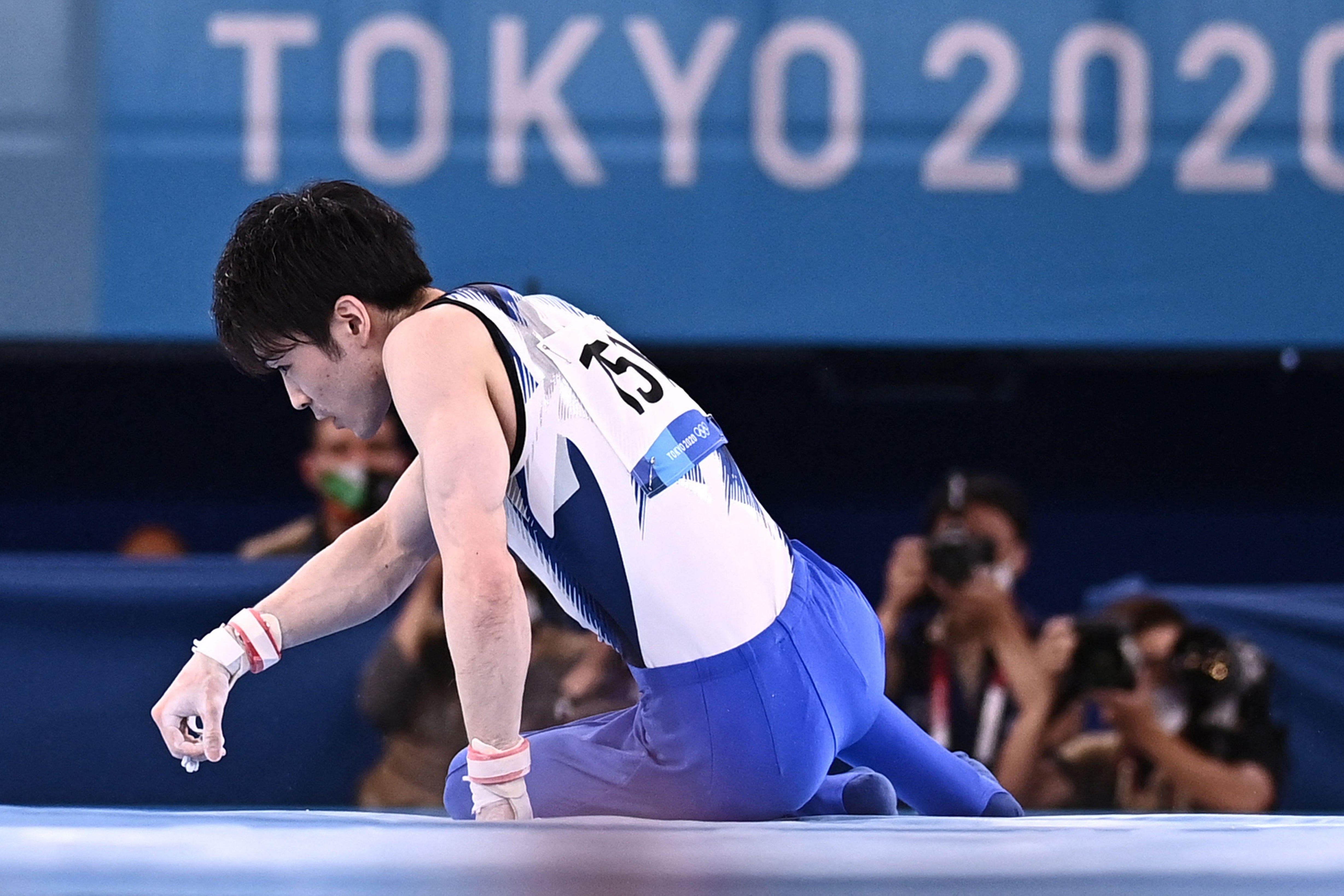 Japan's Kohei Uchimura on the mat looking to the side, a Tokyo 2020 logo in the background