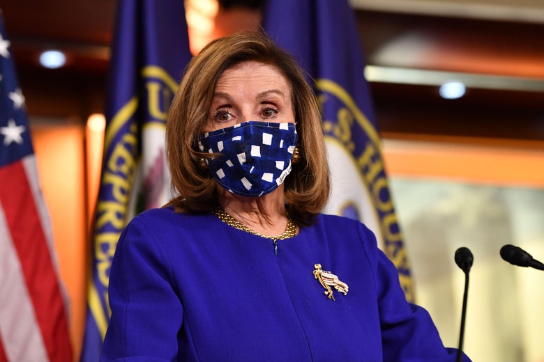 Pelosi stands at a podium wearing a blue checkered mask