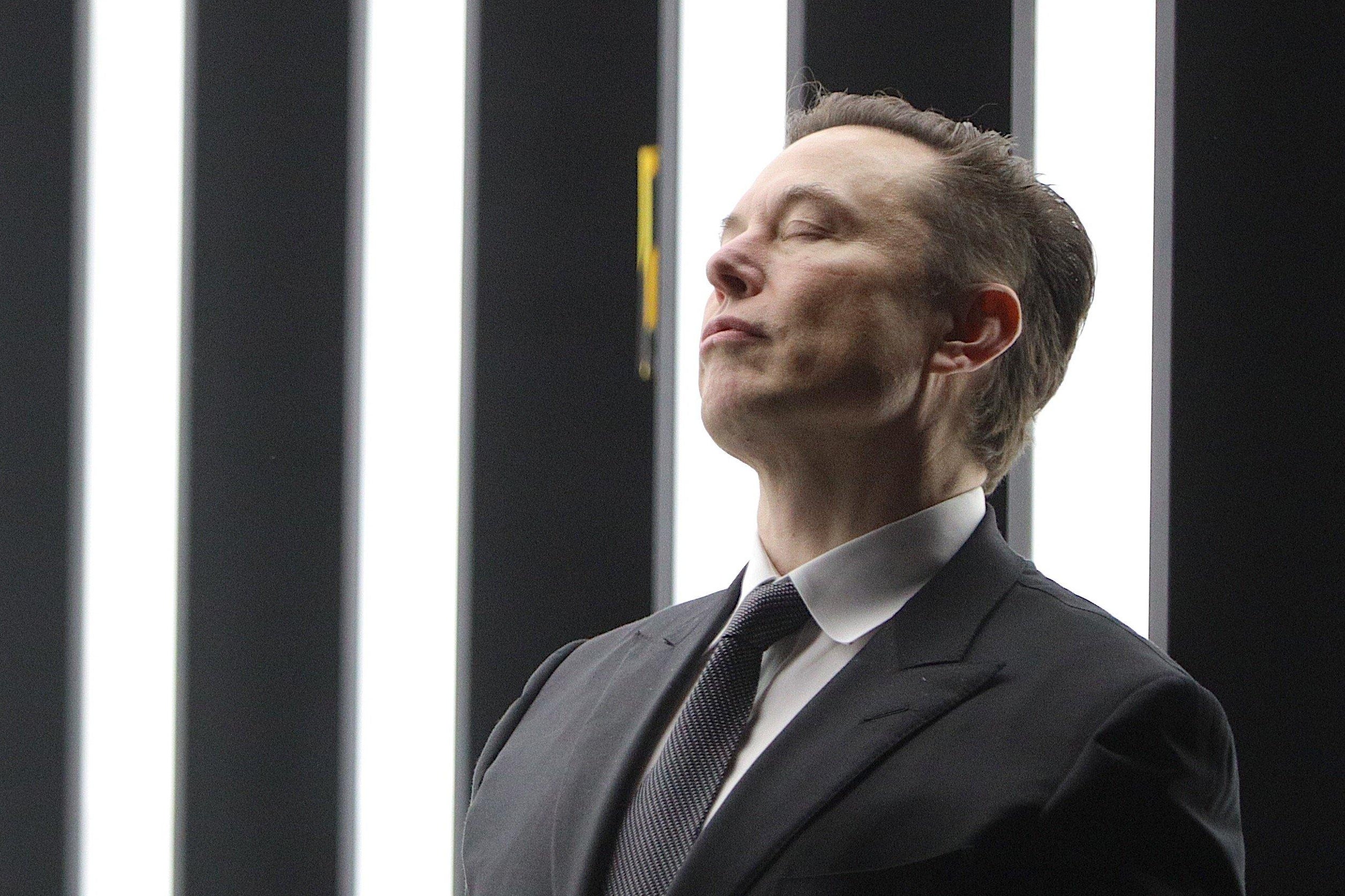 Tesla CEO Elon Musk  leans against a wall with his eyes closed.