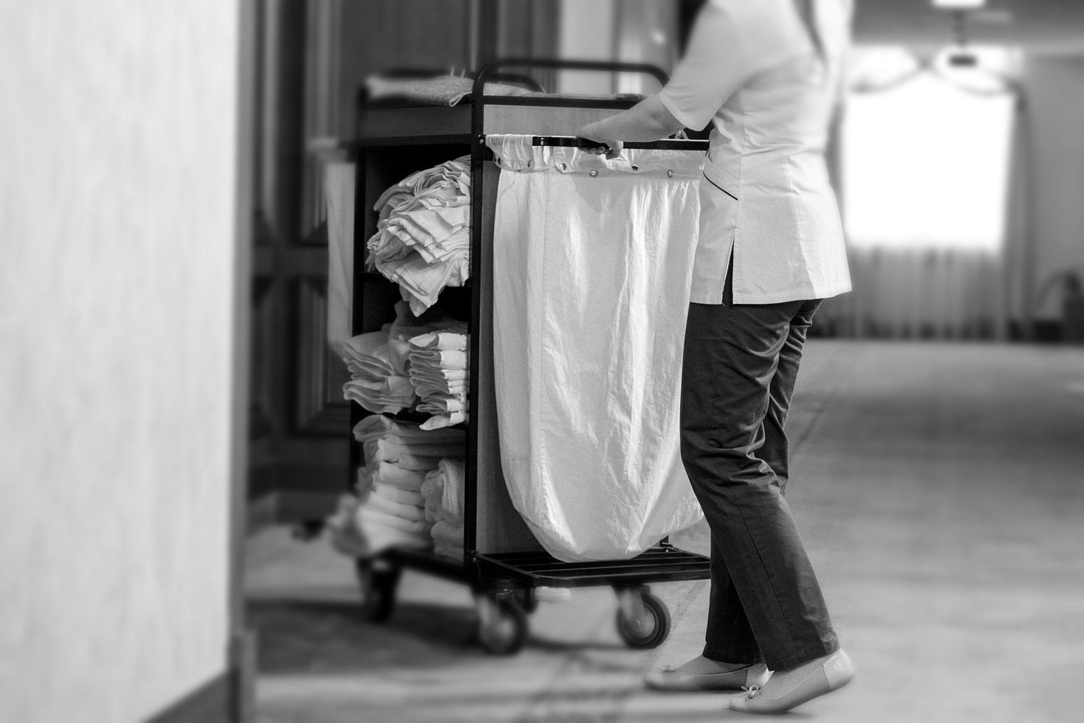 A black-and-white photo of a housekeeper pushing a cart.