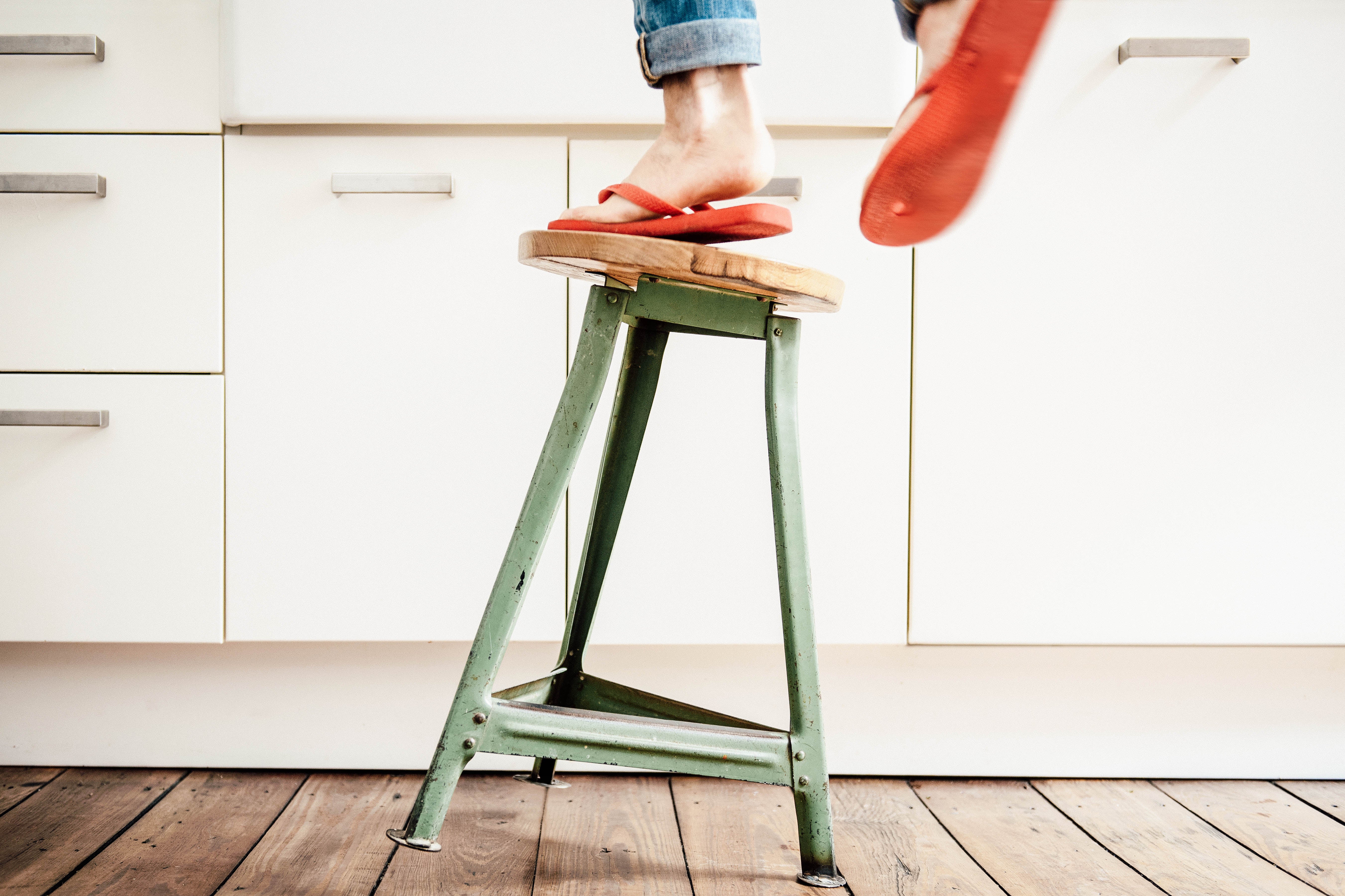 Woman in flip-flops standing on a stool that is tipping over. 