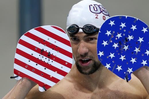 Michael Phelps holding up his hands wearing two paddles: one stripes, one stars