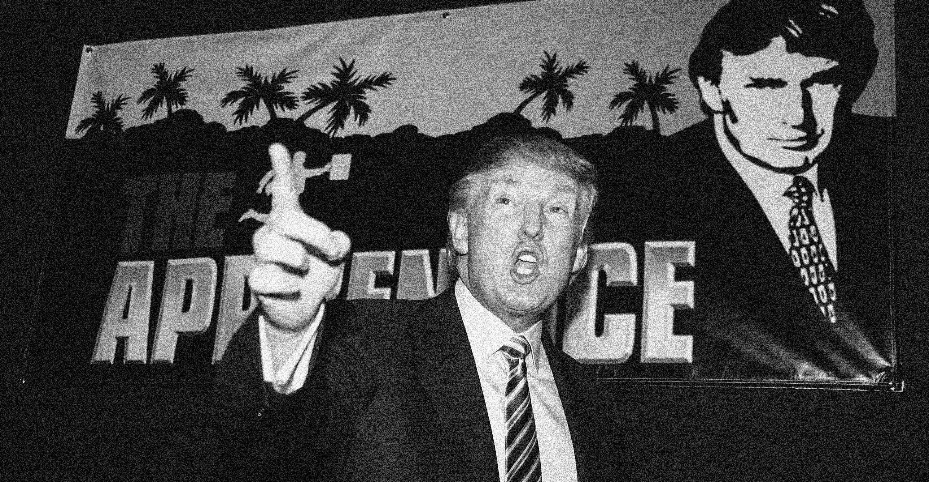 An early 2000s Donald Trump pointing and speaking in front of a promo poster for The Apprentice.