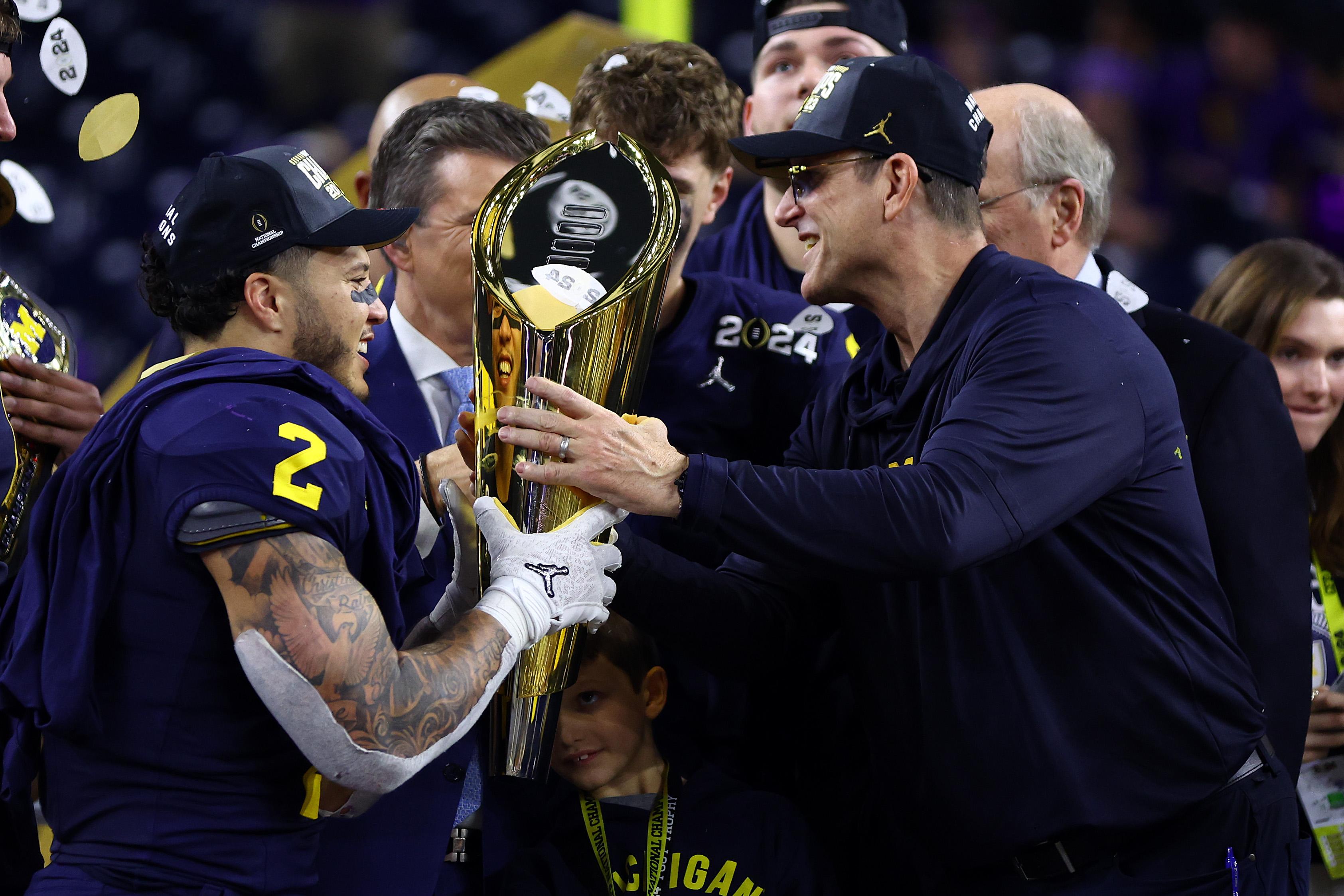 Corum and Harbaugh talk and smile at each other as they hold the trophy together.