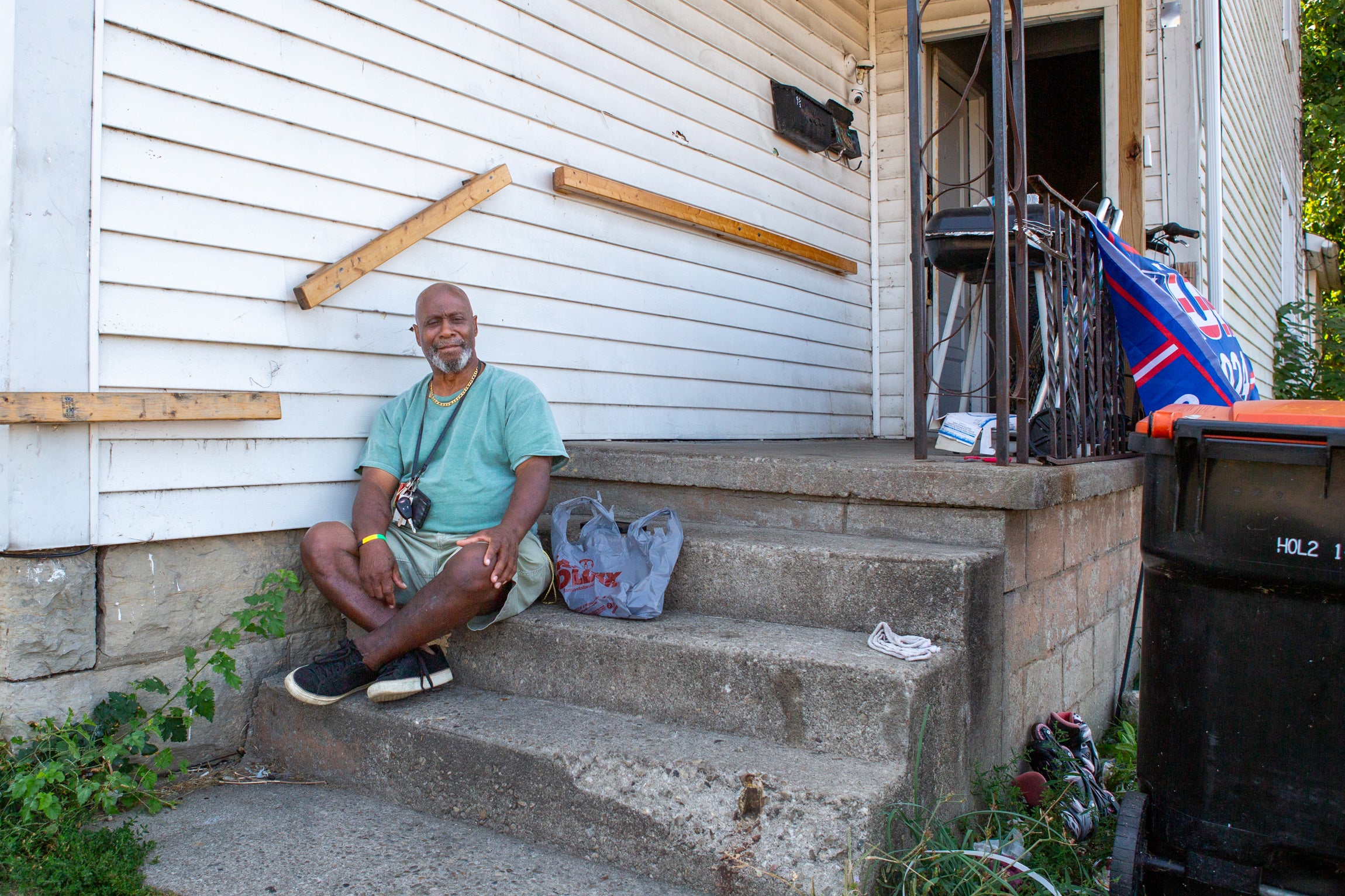 A man sits on his porch next to a Trump flag.