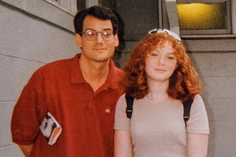 A man in glasses and a red polo shirt smiles as he poses next to a redheaded teenage girl.