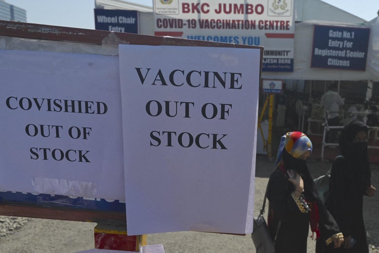 People walk past signs that say "COVISHIELD OUT OF STOCK" and "VACCINE OUT OF STOCK" outside a vaccination center