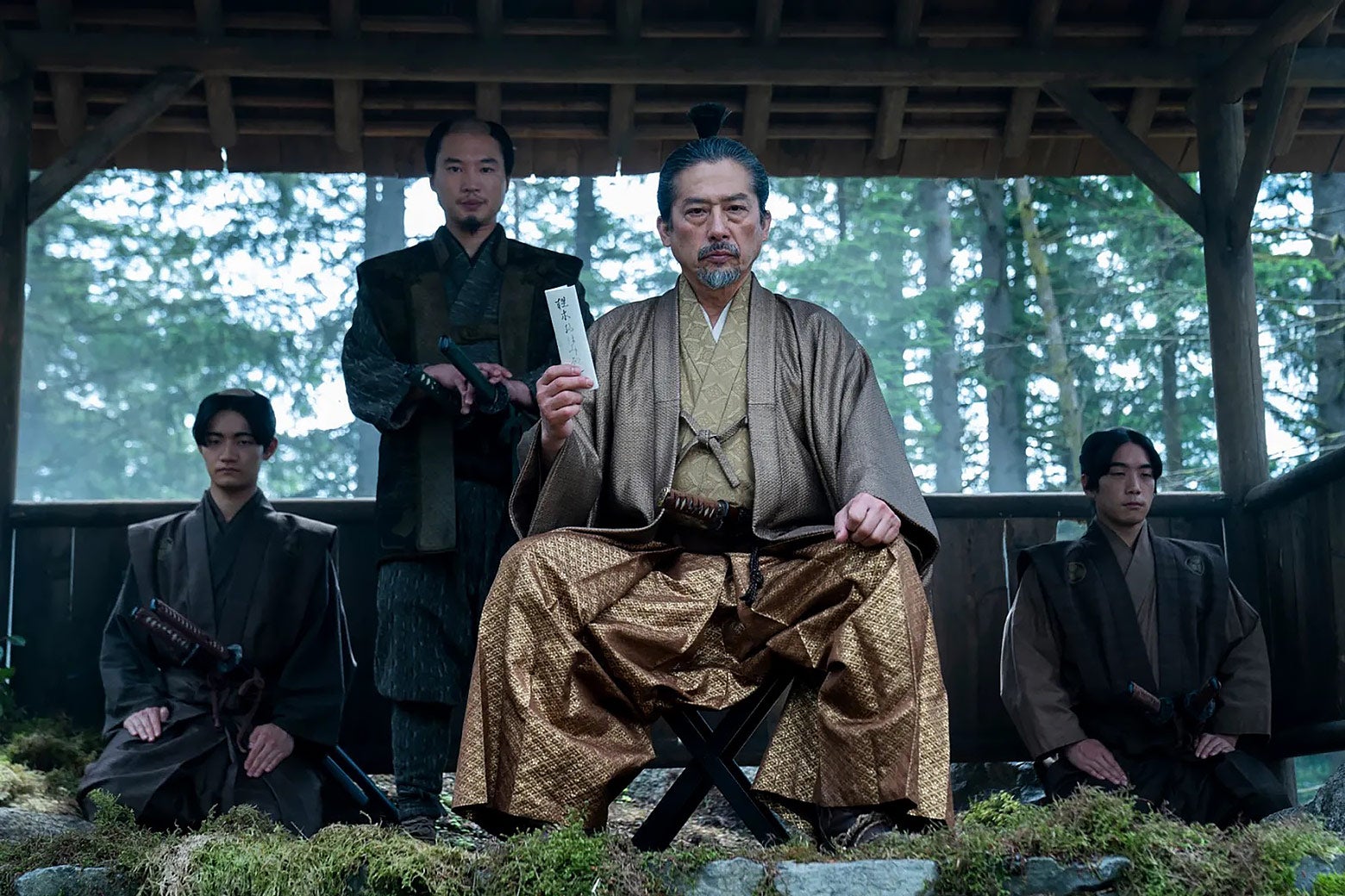 In a scene from Shogun a stern man is speaking while seated on a low stool.