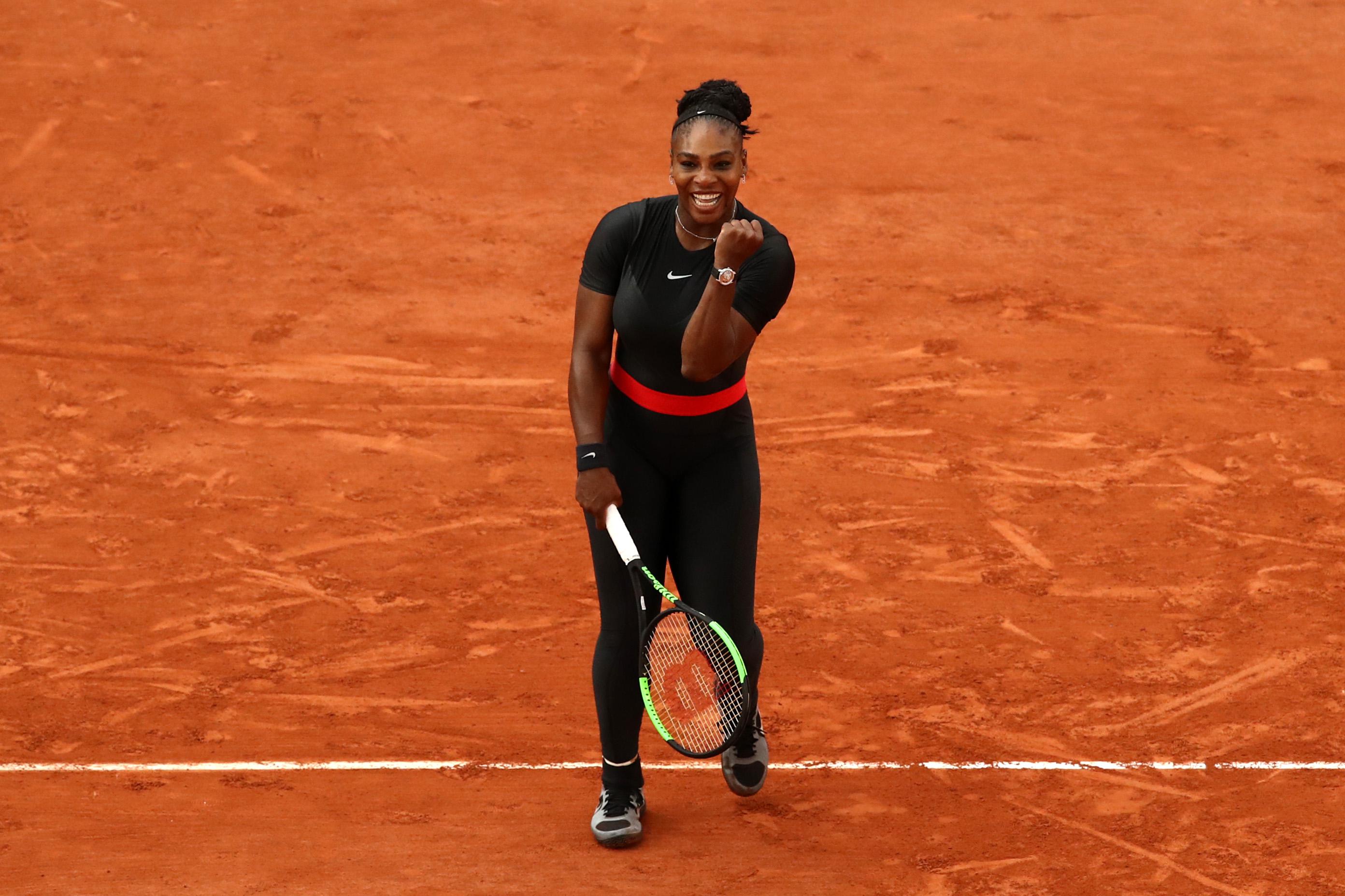 Serena Williams, wearing a black bodysuit, celebrates her victory.