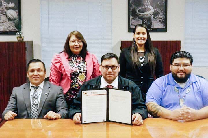 Eddie Crandell (center) and two other men sit at a conference table with two women standing behind them. Crandell holds open an official document.