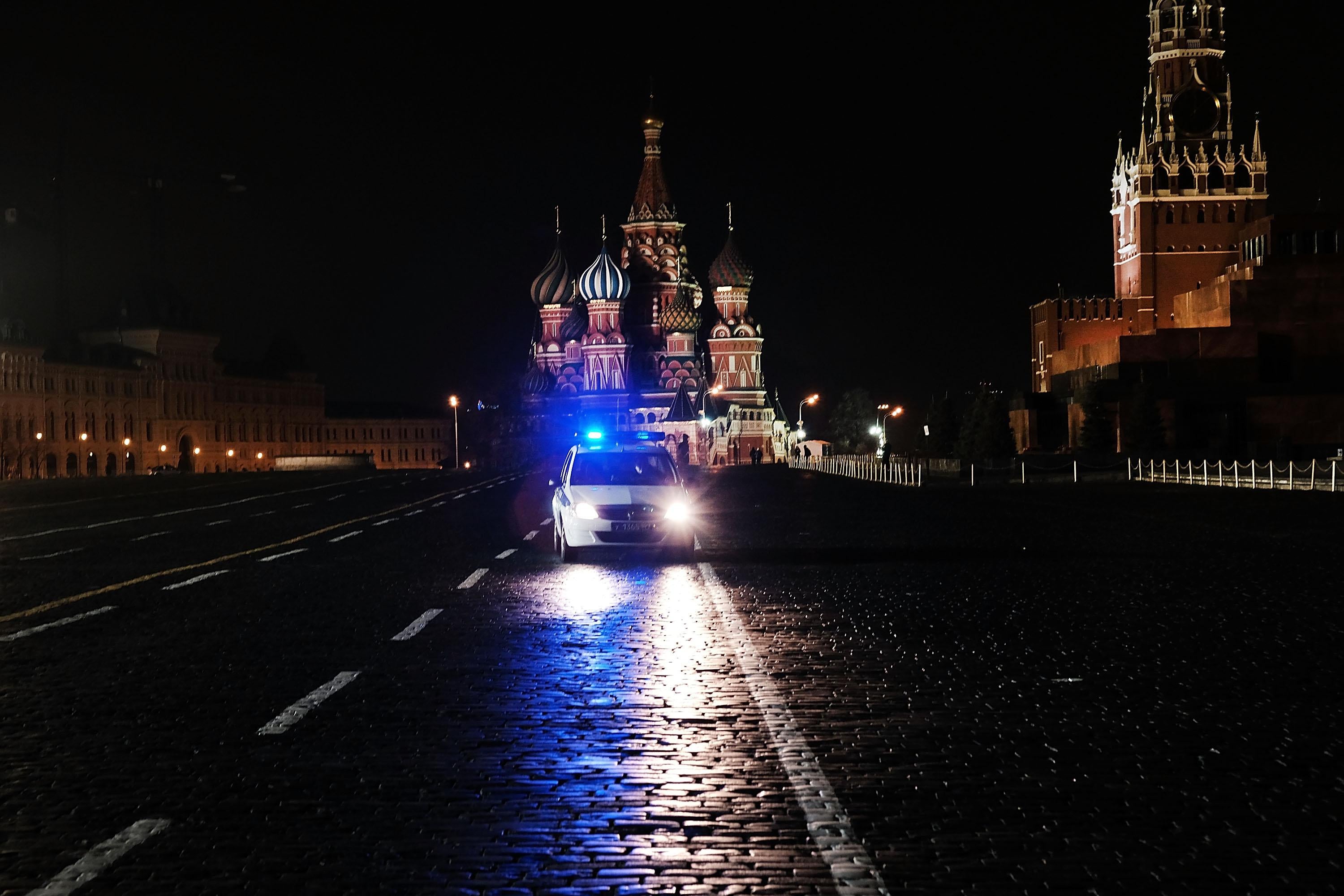 A police vehicle with flashing blue lights in front of Saint Basil's Cathedral at night.