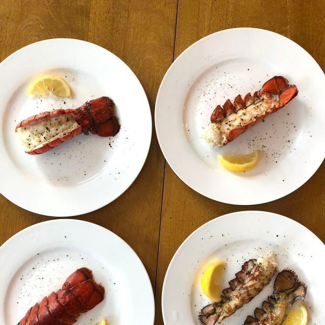 Lobster tails, cooked in different styles, with lemon wedges on four separate plates. 