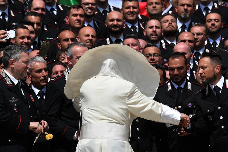 Pope Francis, seen from behind with his cape billowing in the wind, greets a large group of uniformed Carabinieri.