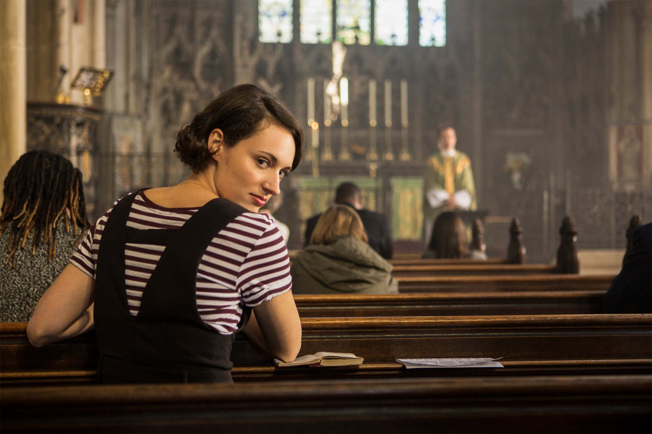In this still from Fleabag, Phoebe Waller-Bridge breaks the fourth wall by staring directly into the camera while sitting in a church pew.