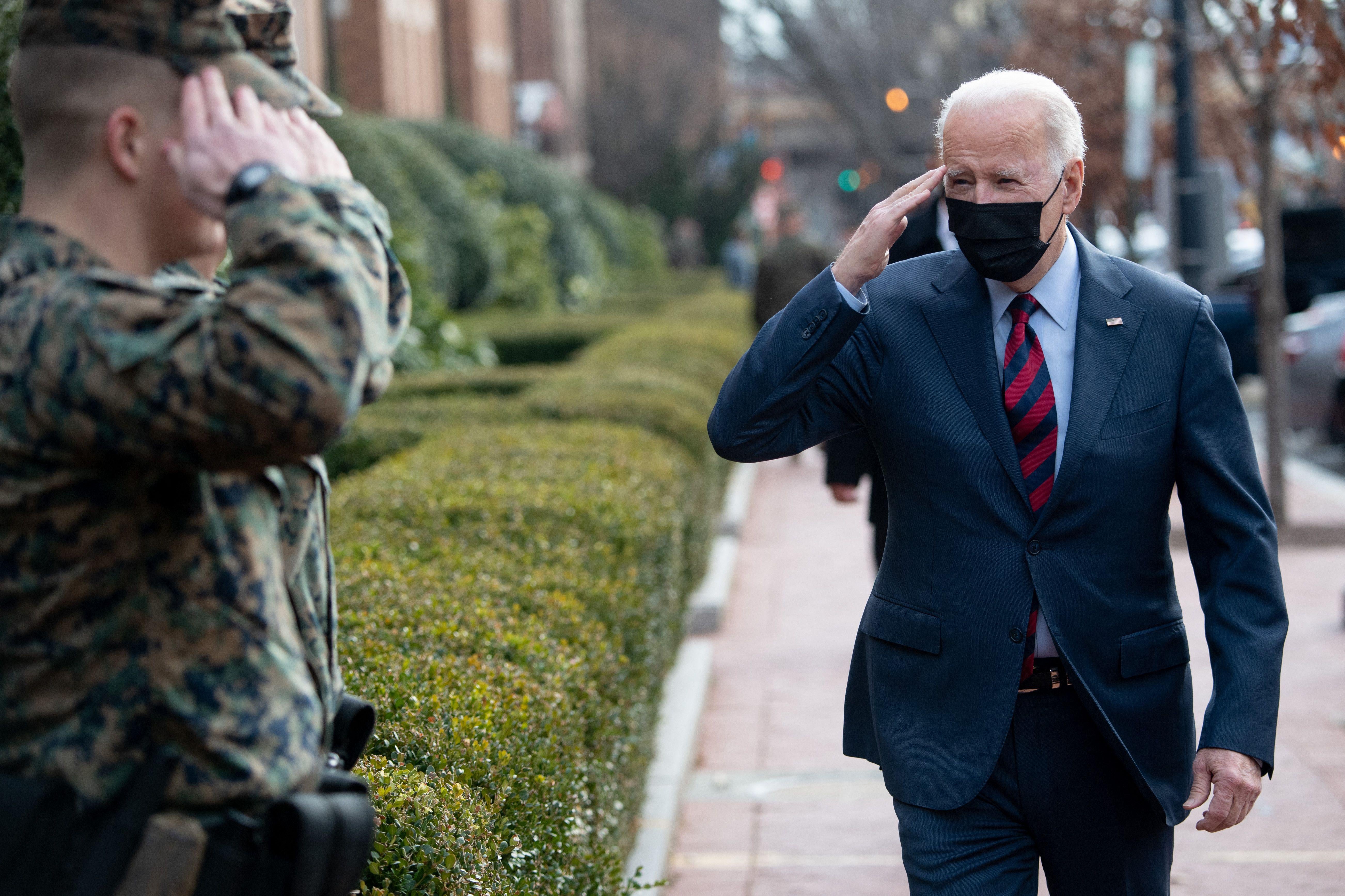 Joe Biden wearing a black mask salutes two Marines on a sidewalk