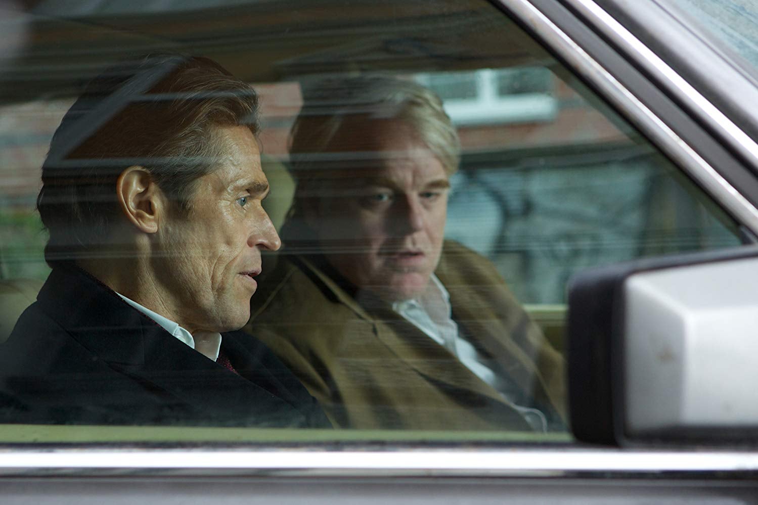 Willem Dafoe and Phillip Seymour Hoffman sit in a car.