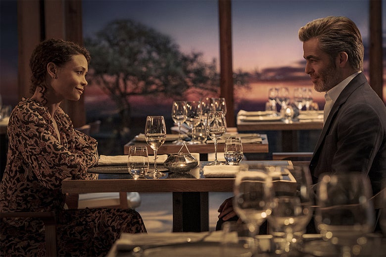 A man and woman look at each other across a restaurant table with wine glasses on it.