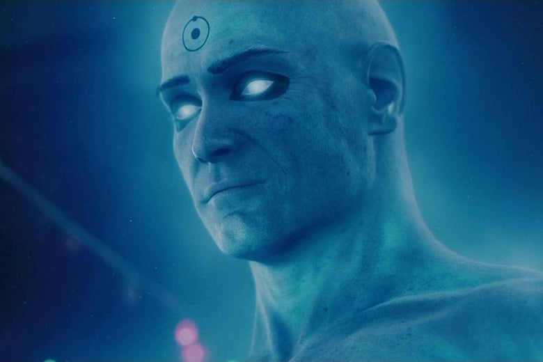 Billy Crudup in entirely blue make-up with Dr. Manhattan's signature symbol on his forehead stares off camera with glowing blue eyes. 
