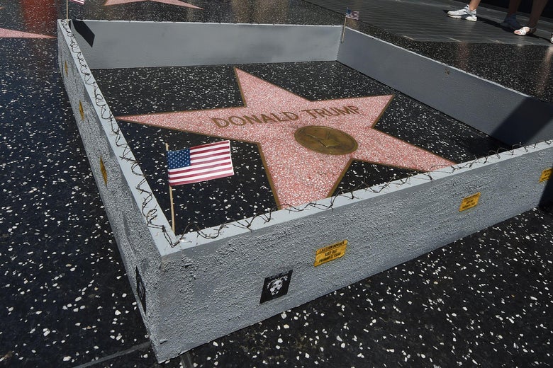 Donald Trump's Hollywood Walk of Fame star enclosed by a tiny gray fence topped with barbed wire and an American flag in one corner.
