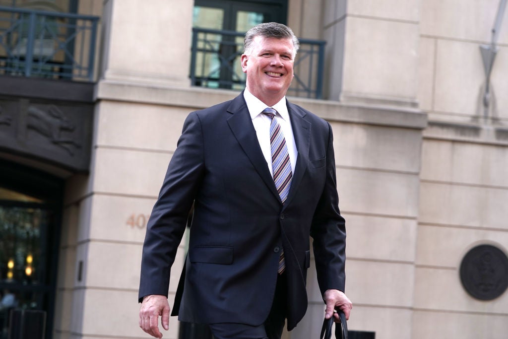 A grinning lawyer with salt-and-pepper hair and a strong jawline walks away from a courthouse.