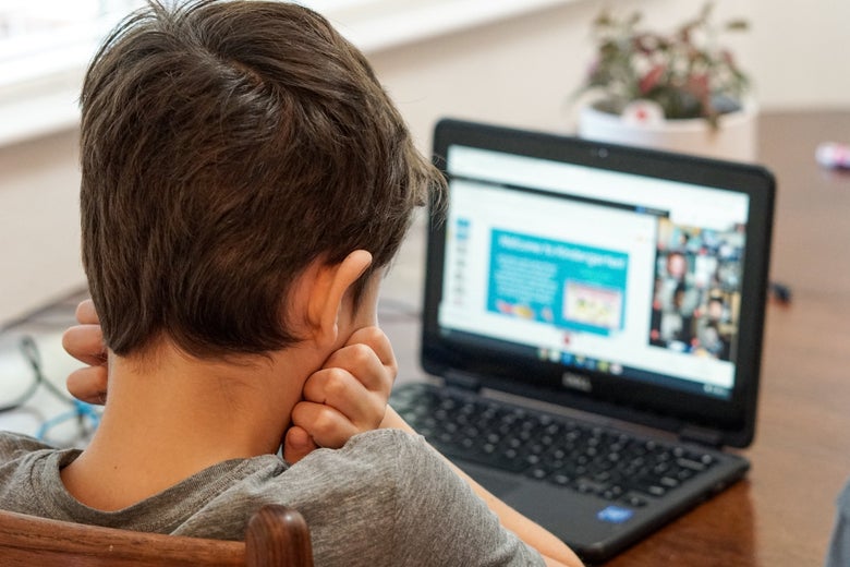 A view from the back and above as a child looks at a laptop with his chin in his hands.
