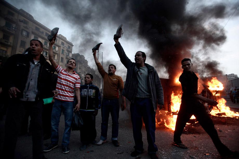 Egyptian anti-Morsi protesters hold up their shoes near a burning police vehicle in Tahrir Square during a march against a visit by U.S. Secretary of State John Kerry on March 3, 2013 in Cairo, Egypt.