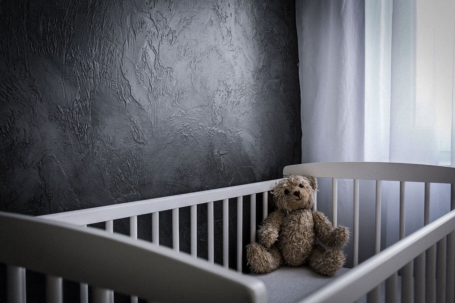 An empty crib, with a teddy bear inside it.