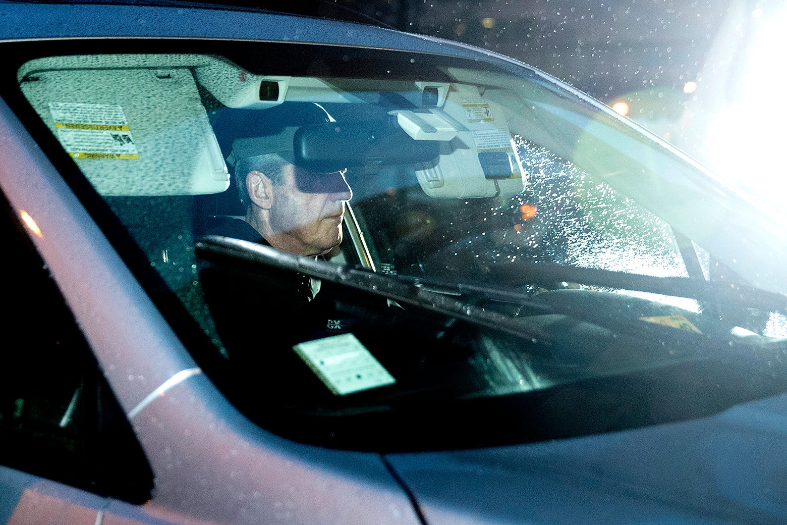 Muller is seen through the windshield of a car in the rainy pre-dawn dark.