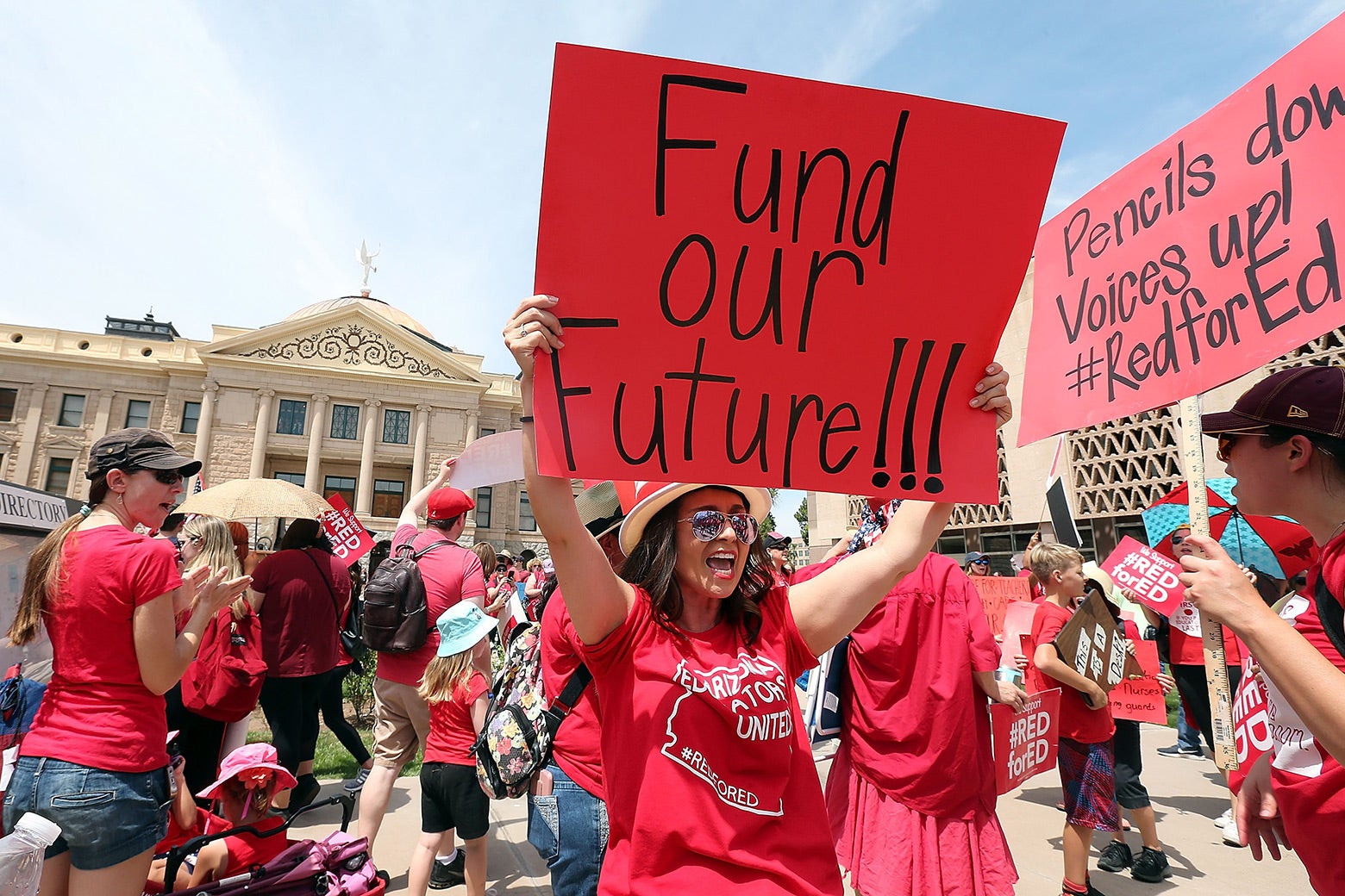 Teachers wear red T-shirts and hold signs that say things like, "Fund our future!!!"