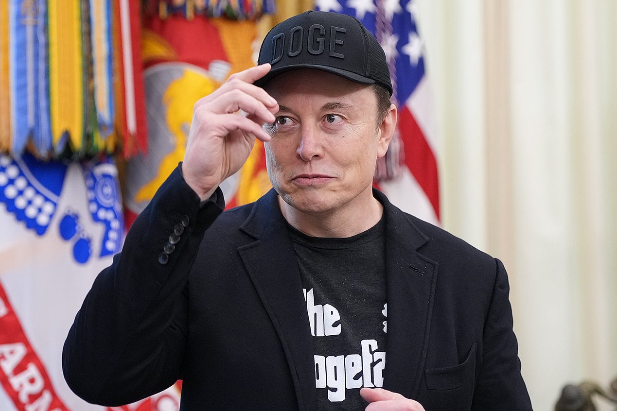 Musk in the Oval Office, wearing a black DOGE hat and black T-shirt that reads "The Dogefather."