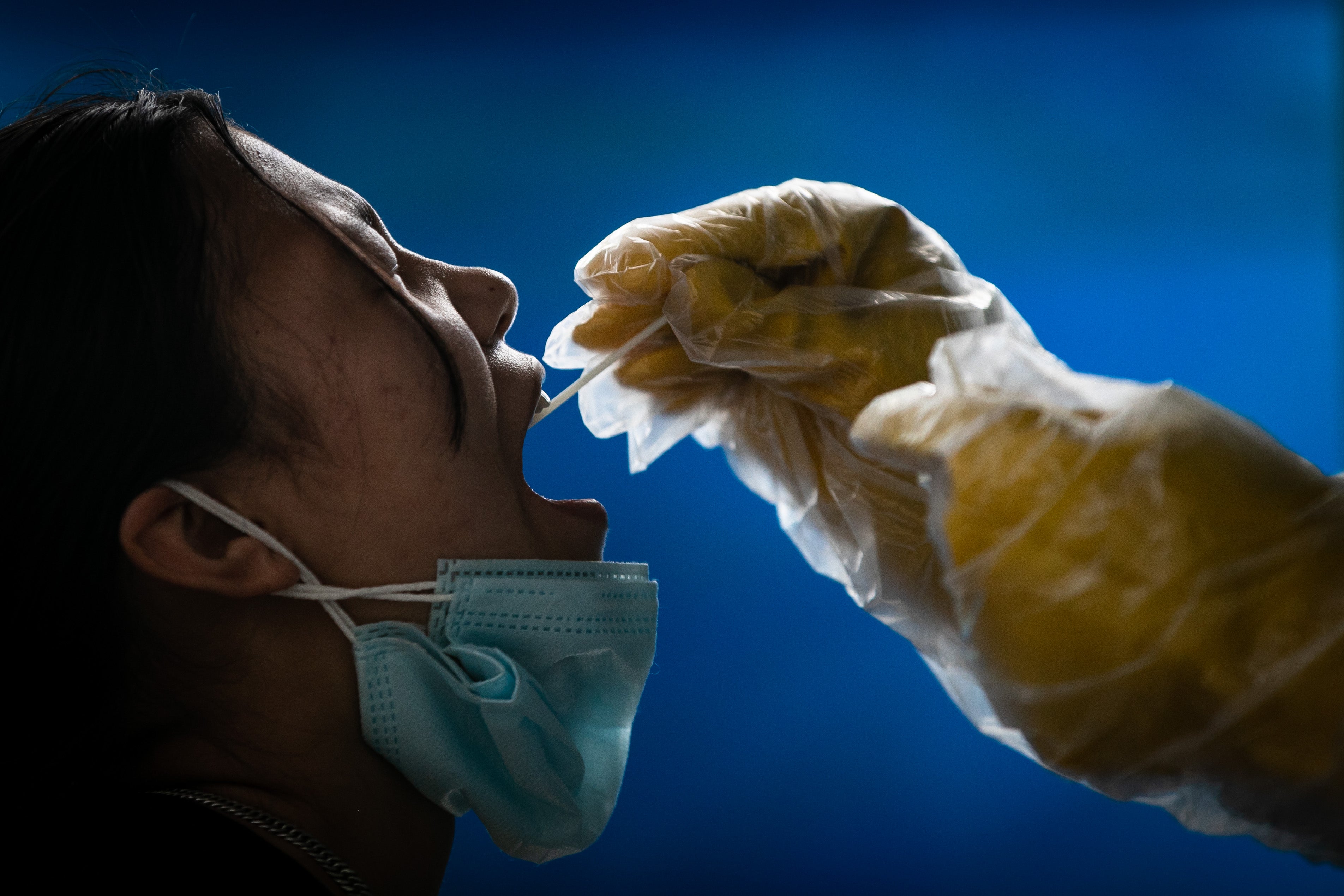 Close-up of a woman with eyes closed and mouth agape as a gloved hand holds a swab into her mouth.