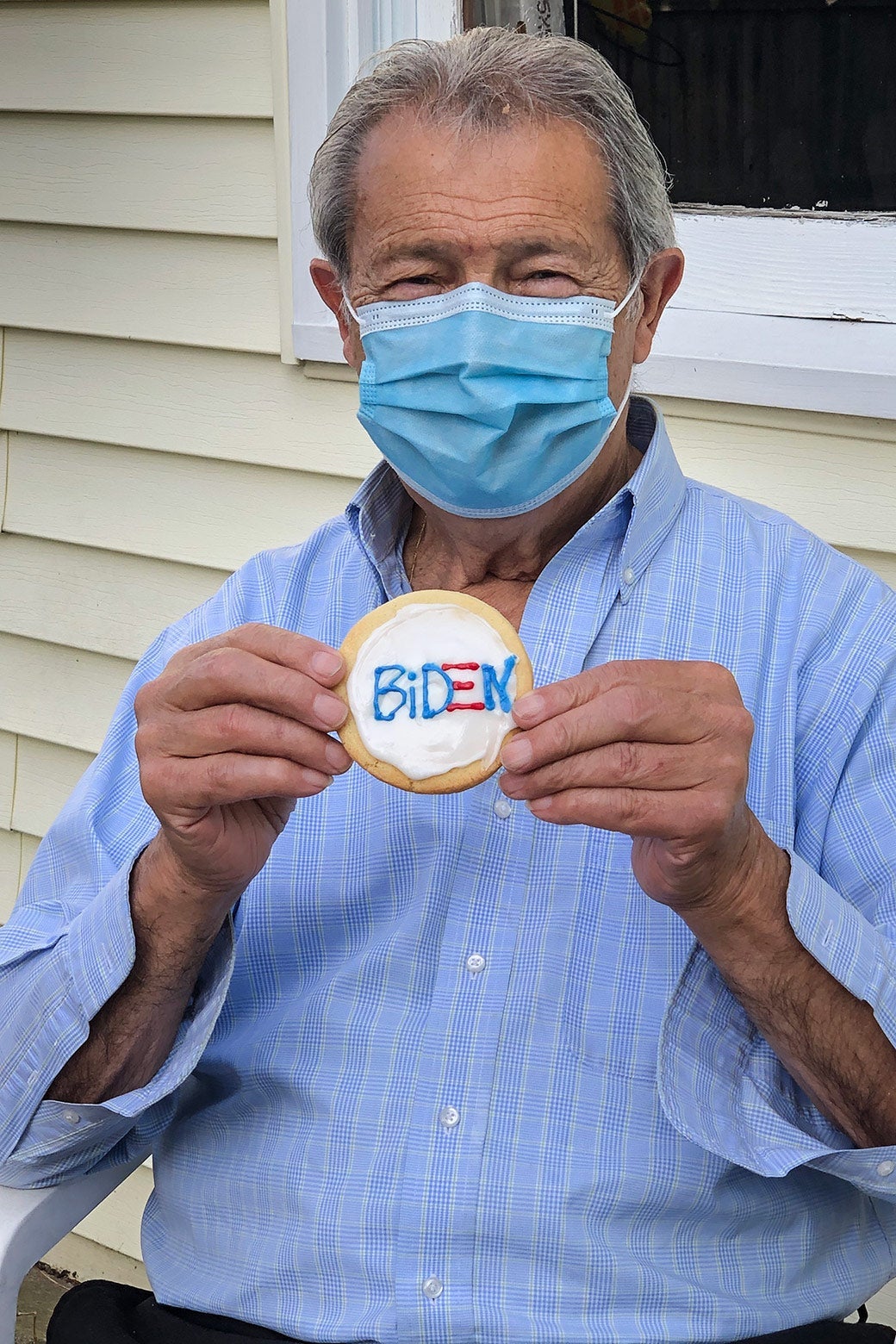 Pasquale wearing a mask and holding a cookie that says Biden on it.