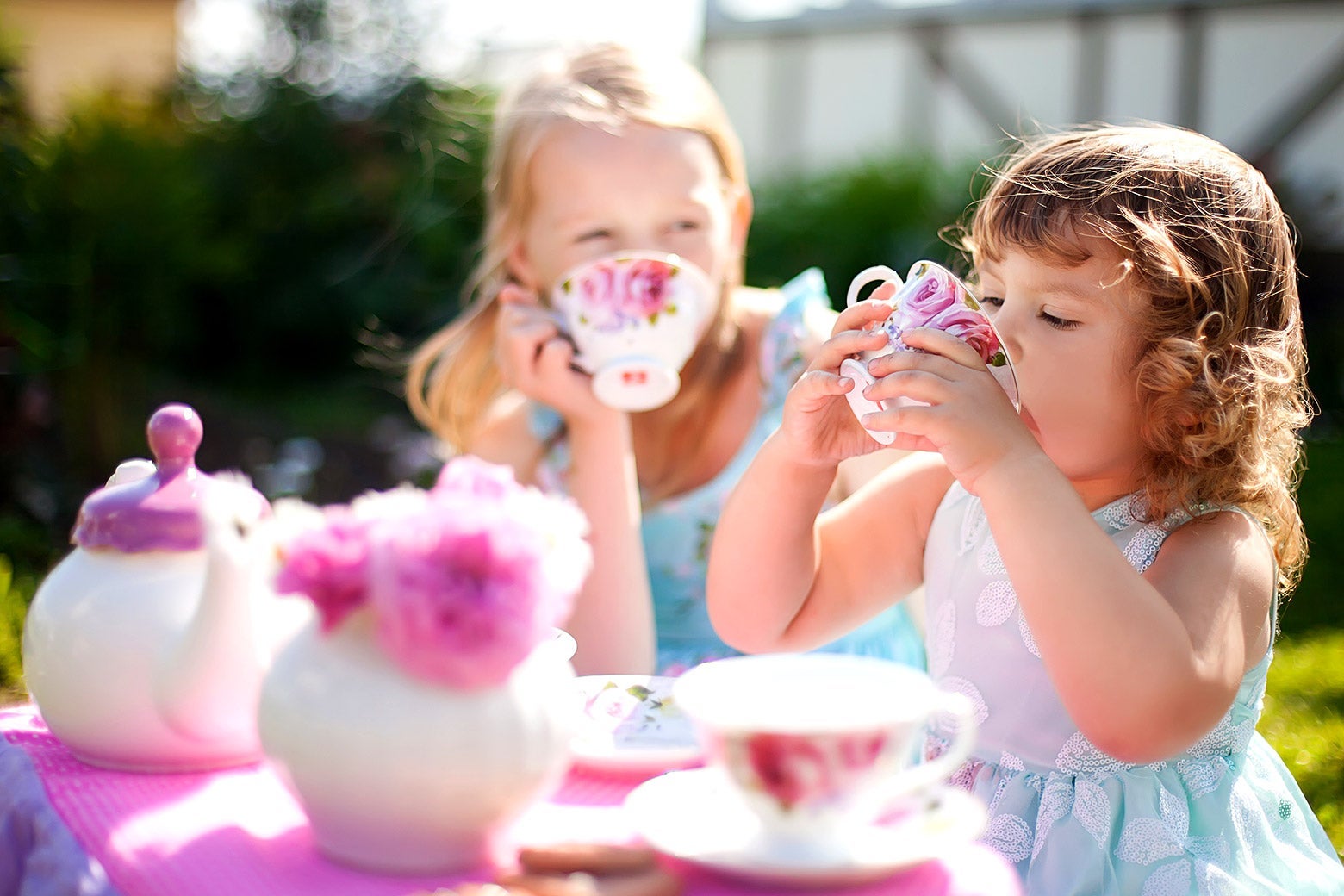 Two young girls dressed like princesses have a tea party