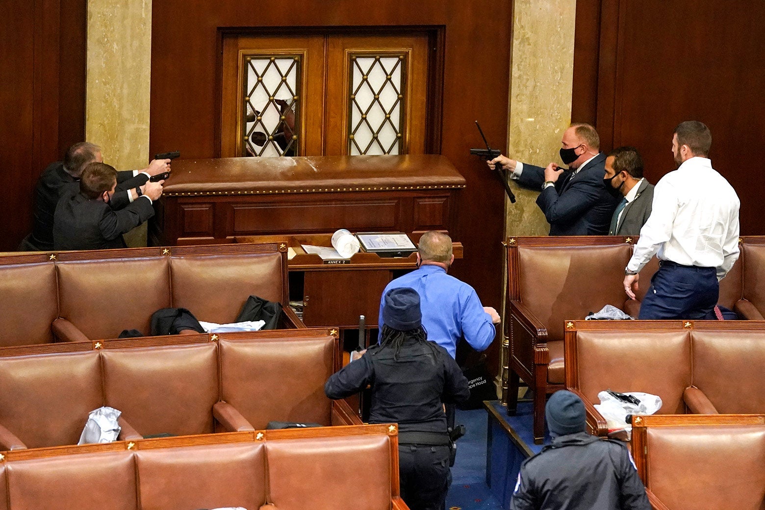 Three Capitol police officers inside the House Chamber point their gun at a door.