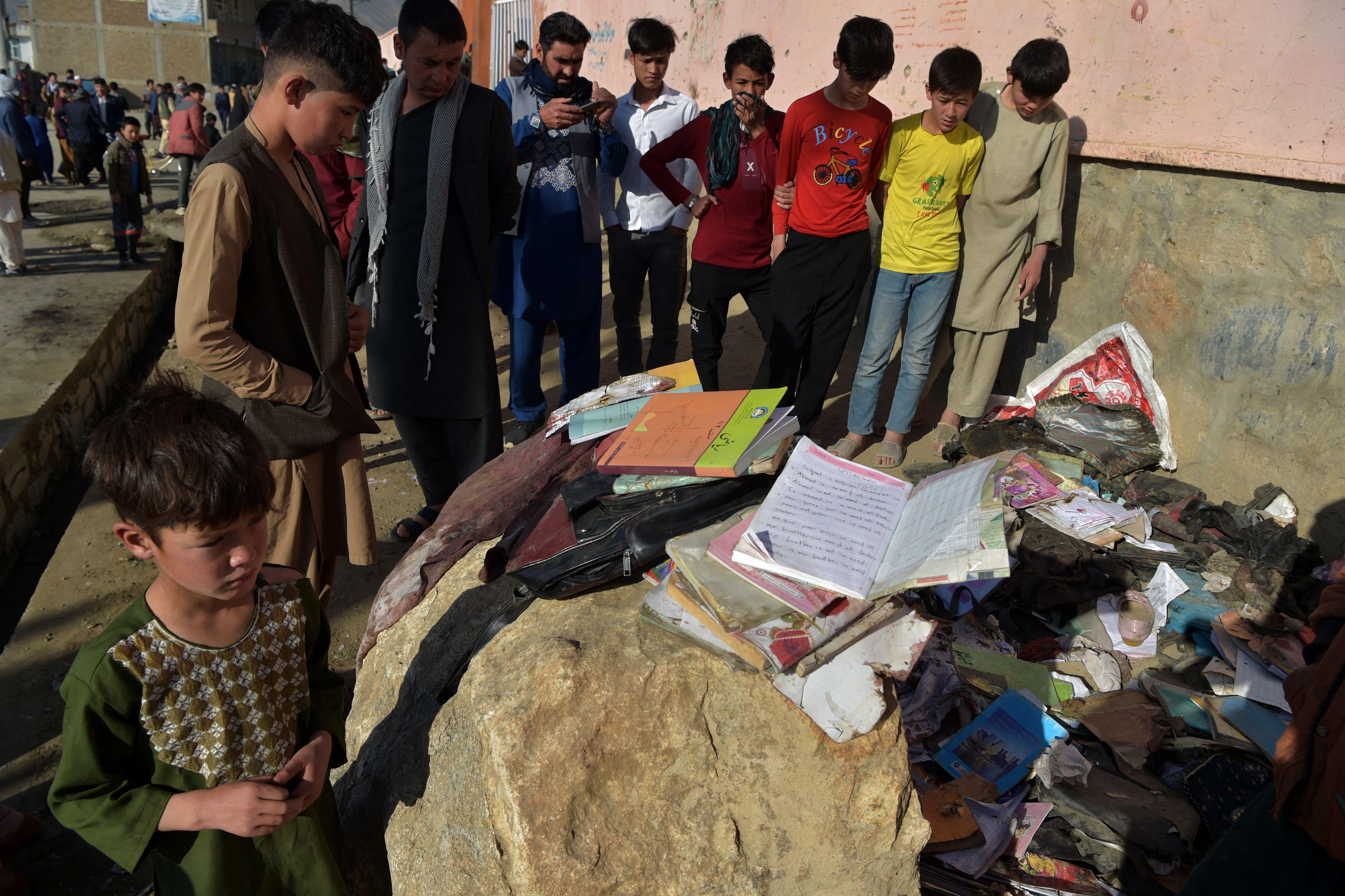 Onlookers stand next to the backpacks and books of victims following yesterday's multiple blasts outside a girls' school in Dasht-e-Barchi on the outskirts of Kabul on May 9, 2021.