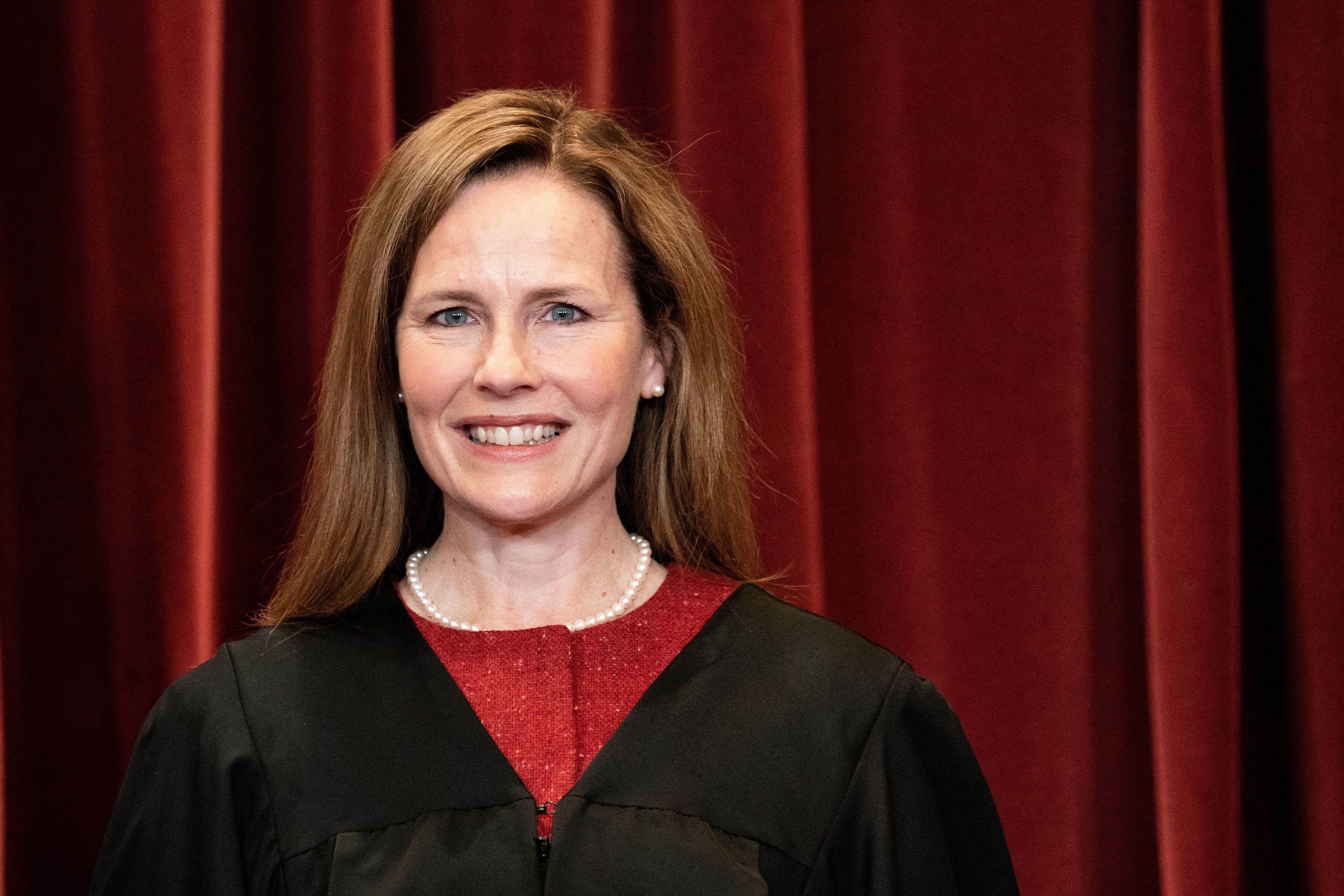Justice Amy Coney Barrett wearing a robe during the group photo in front of a red velvet curtain.