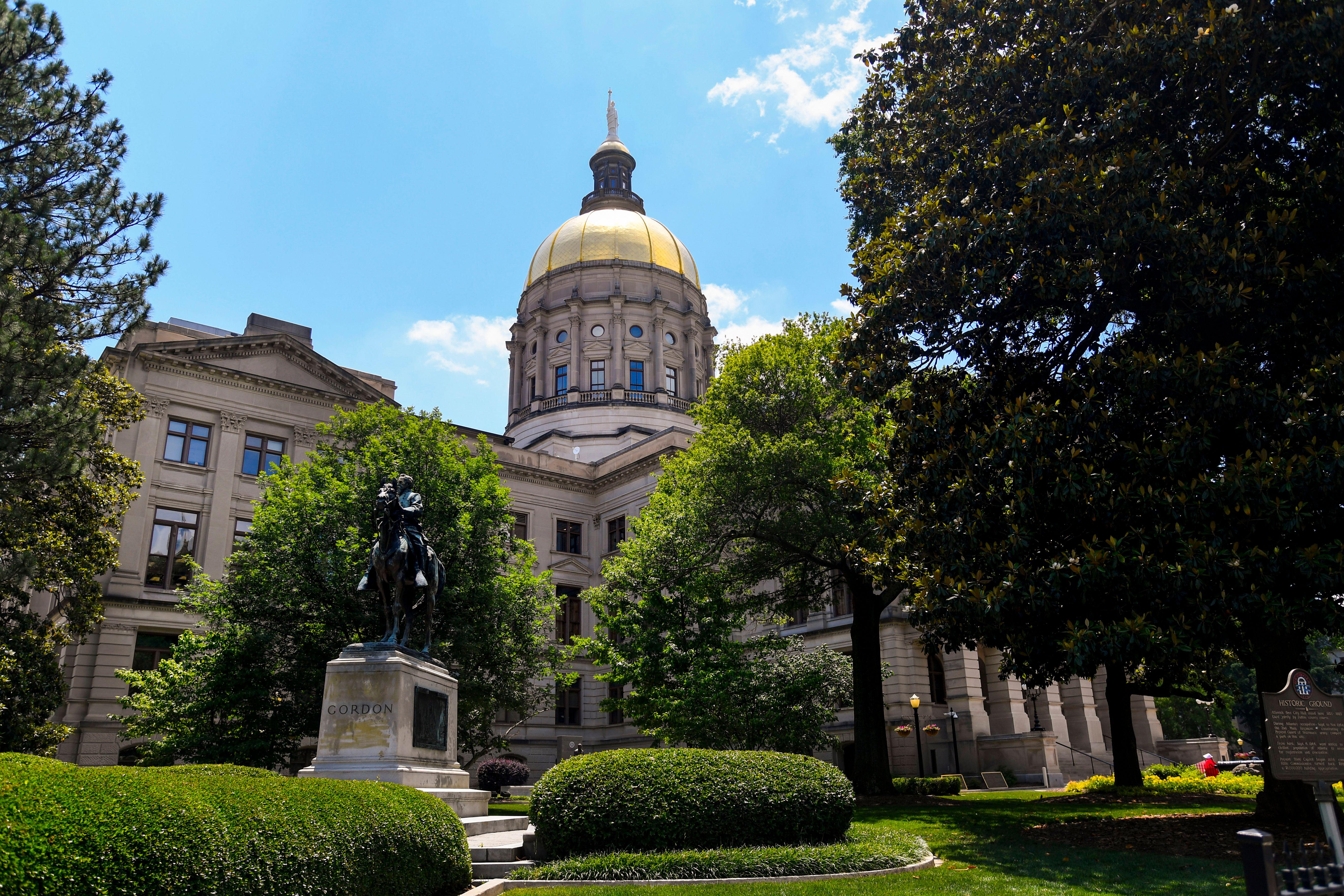 A 19th-century building surrounded by greenery and a statue.