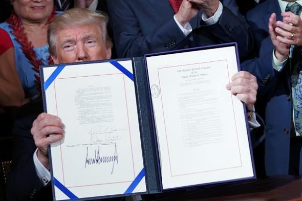 Trump holds up a big ceremonial bill at a signing ceremony.