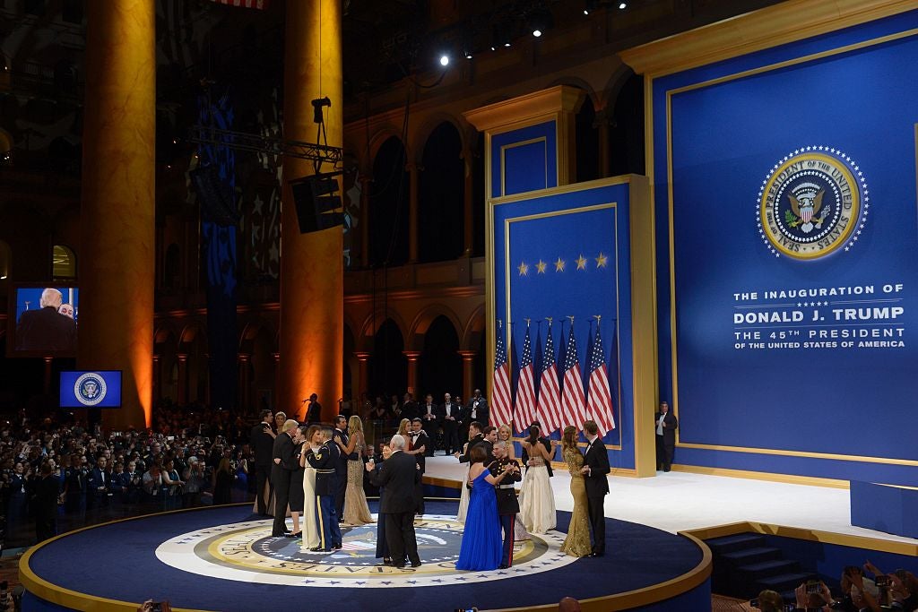 A wide shot of Donald and Melania Trump and several other couples dancing on a stage in a large hall with high ceilings.
