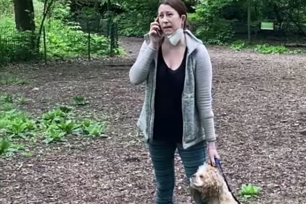 White woman making a cellphone call in the park while holding her dog by its leash