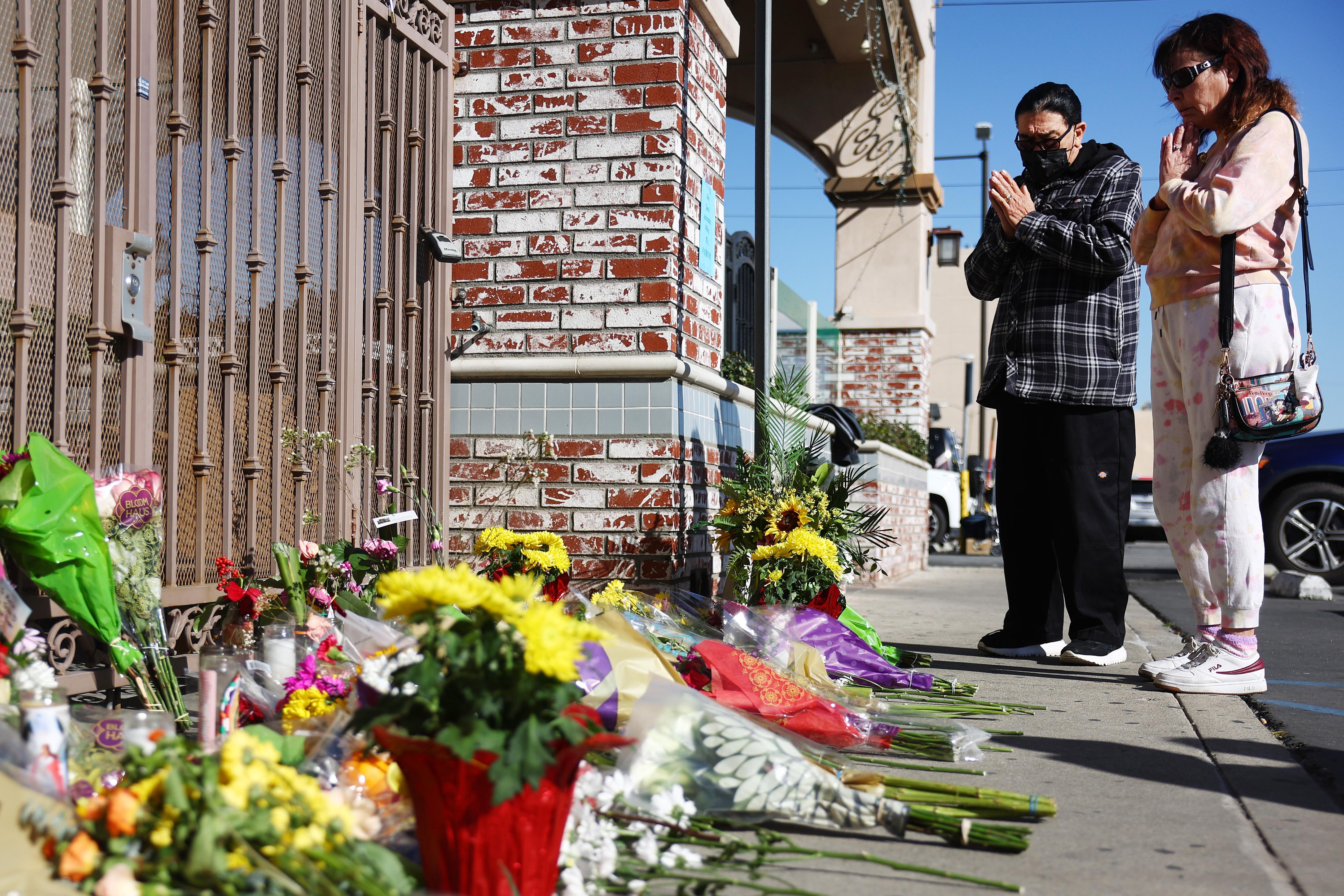 Two people stand outside in front of a makeshift memorial outside a ballroom dance studio.