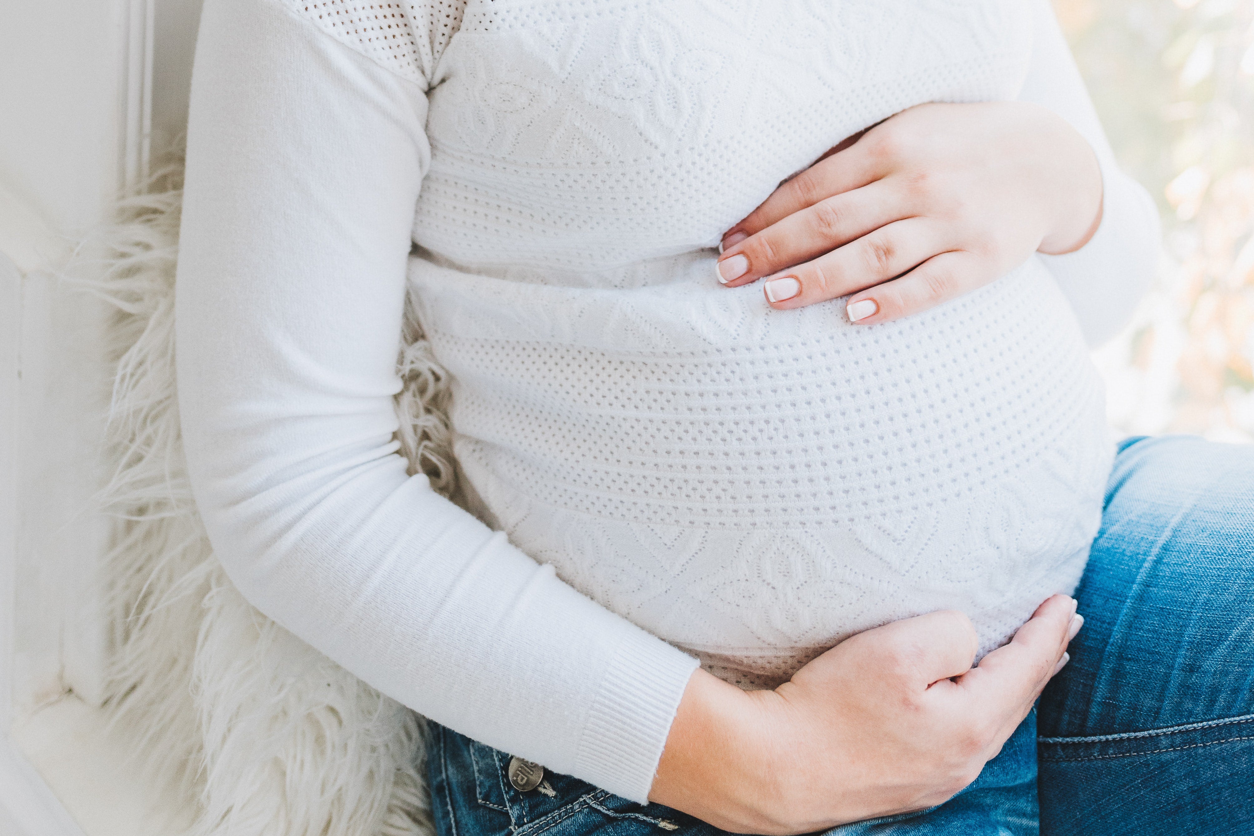 A pregnant person with a white long-sleeve shirt and their hands on their belly. 