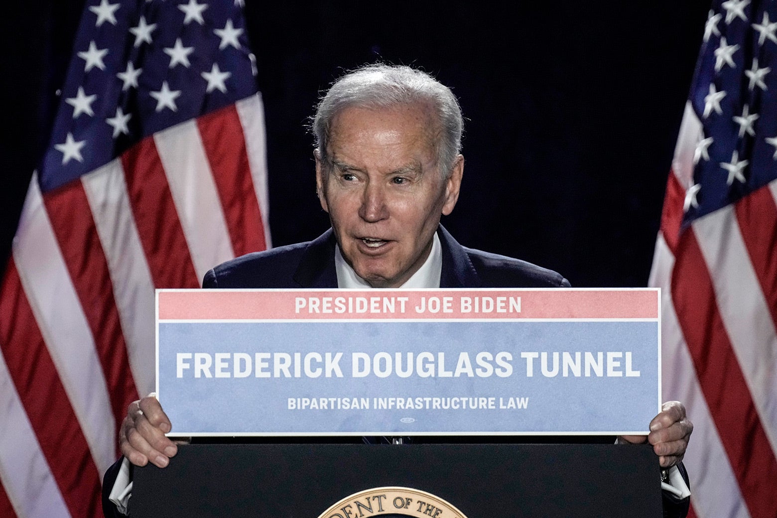 President Biden holds up a sign that reads "Frederick Douglass Tunnel" with a huge grin on his face.