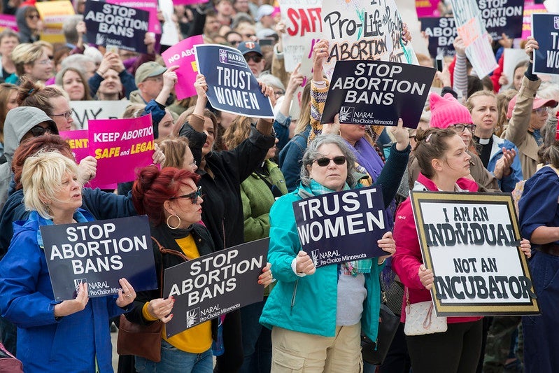 Women holds signs promoting the right to abortion access, including "trust women."