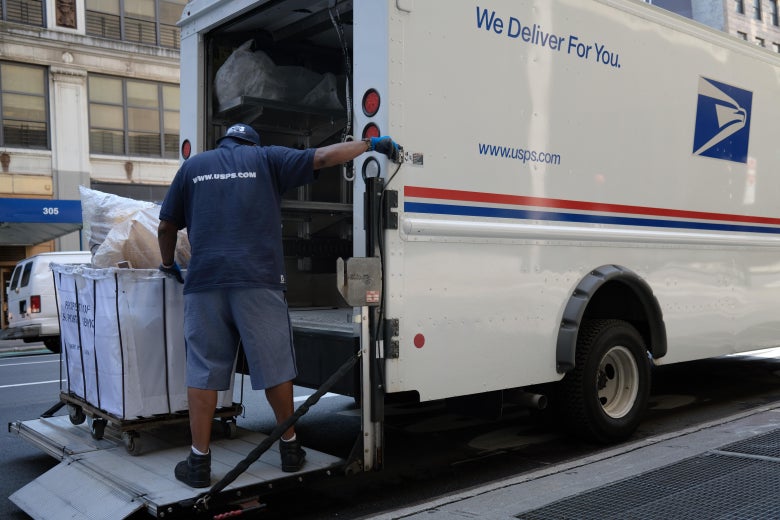 A postal worker loads mail into a USPS truck.