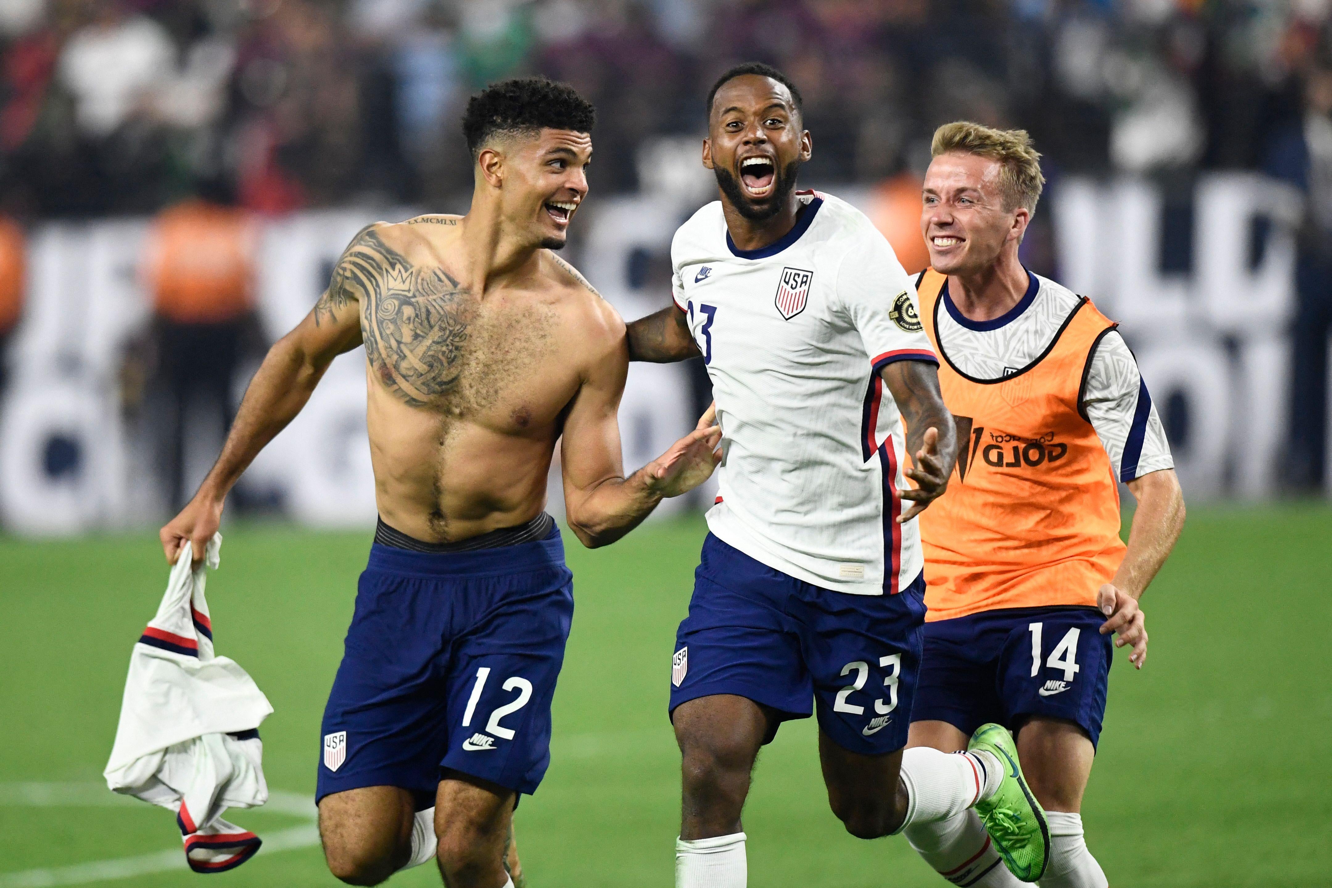 Shirtless and tattooed Miles Robinson, screaming Kellyn Acosta, and smiling Jackson Yueill run, embrace, and celebrate on the pitch.