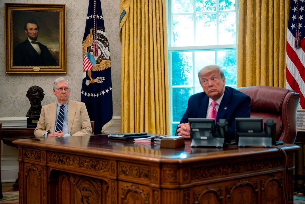 Trump, seated behind his desk, turns his head to listen to another speaker as McConnell looks on from a chair.