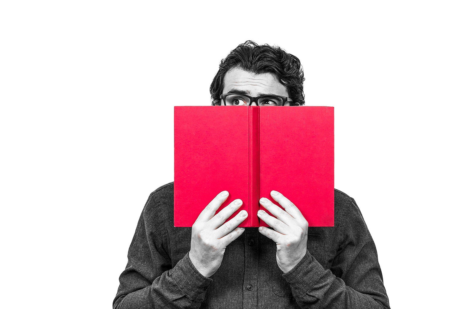 Man wearing glasses hiding behind a book.